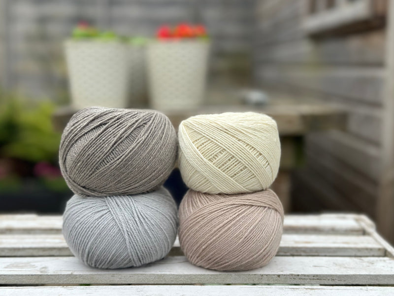 Four balls of wool in medium grey, cream, silvery grey, and oatmeal beige.