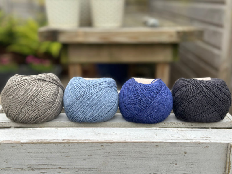 Four balls of wool in mid-grey, medium denim blue, royal blue, and dark grey.