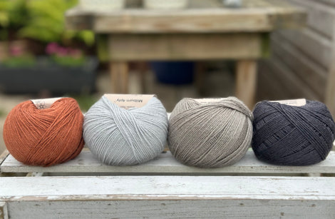 Four balls of wool in rust, silvery grey, medium grey, and dark grey.