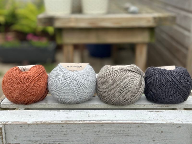 Four balls of wool in rust, silvery grey, medium grey, and dark grey.