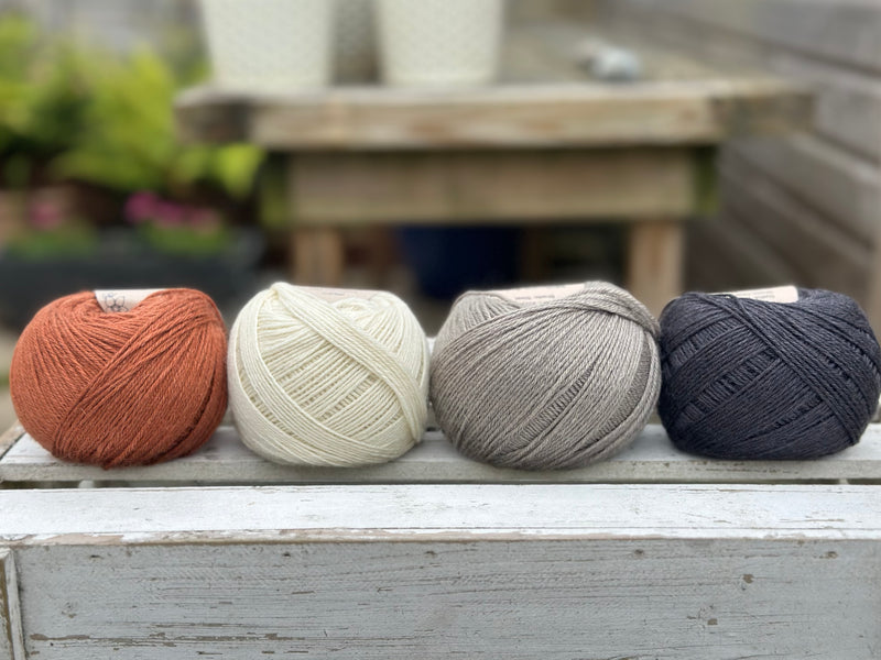 Four balls of wool in rust, cream, mid grey and dark grey.