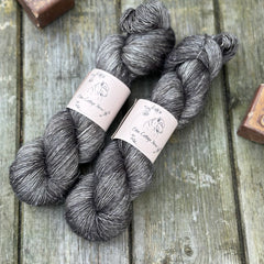 Two skeins of dark grey yarn with pale slubs running through them