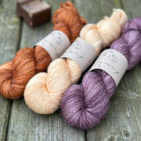 Three skeins of yarn. From left to right - an orangey brown skein, a pale orange skein and a purple skein