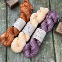 Three skeins of yarn. From left to right - an orangey brown skein, a pale orange skein and a purple skein