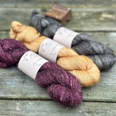 Three skeins of yarn. From left to right: a dark purple skein, a golden brown skein and a dark grey skein