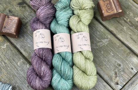 Three skeins of yarn. From left to right: a purple skein, a turquoise skein and a green skein