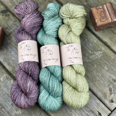 Three skeins of yarn. From left to right: a purple skein, a turquoise skein and a green skein