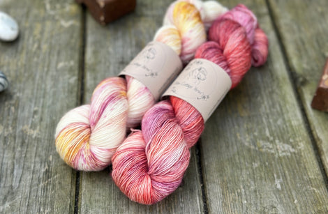 Two skeins of yarn. One variegated cream, yellow and pink skein. One variegated red, pink and purple skein
