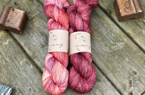 Two skeins of yarn in shades of reddish-purple, pink and orange