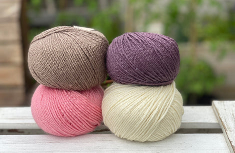 Four balls of yarn in two rows of two balls. There is a bright pink ball, a cream ball, a brown ball and a dark purple ball