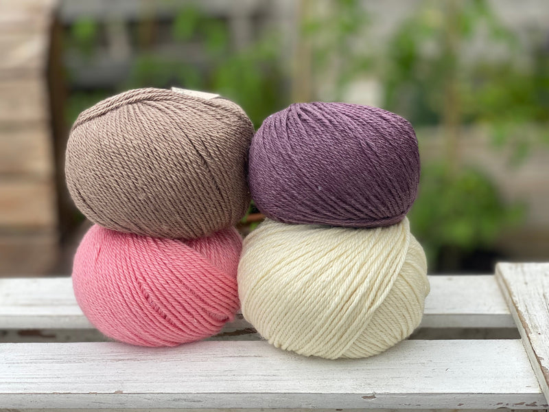 Four balls of yarn in two rows of two balls. There is a bright pink ball, a cream ball, a brown ball and a dark purple ball