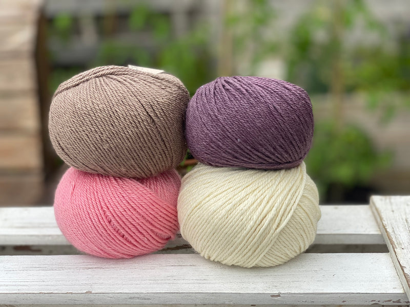 Four balls of yarn in two rows of two balls. There is a bright pink ball, a cream ball, a brown ball and a dark purple ball
