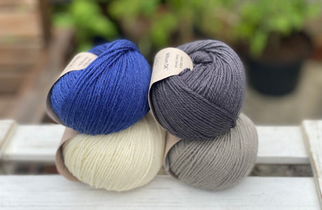 Four balls of yarn in two rows of two balls. There is a deep blue ball, a cream ball, a grey ball and a dark grey ball