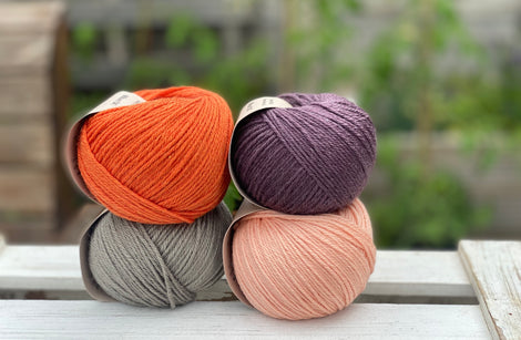 Four balls of yarn in two rows of two balls. There is an orange ball, a dark purple ball, a grey ball and a peachy orange ball