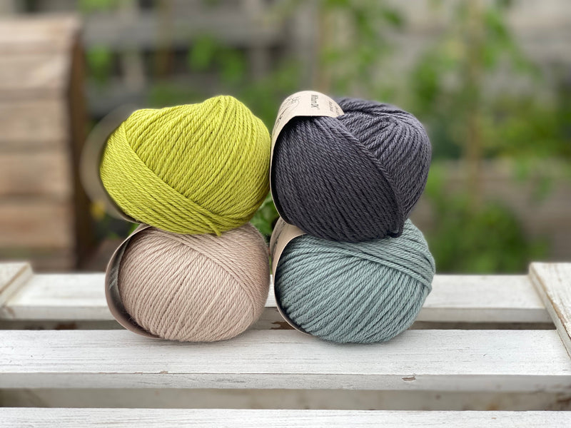 Four balls of yarn in two rows of two. There is a green ball, a dark grey ball, a beige ball and a blue-green ball.