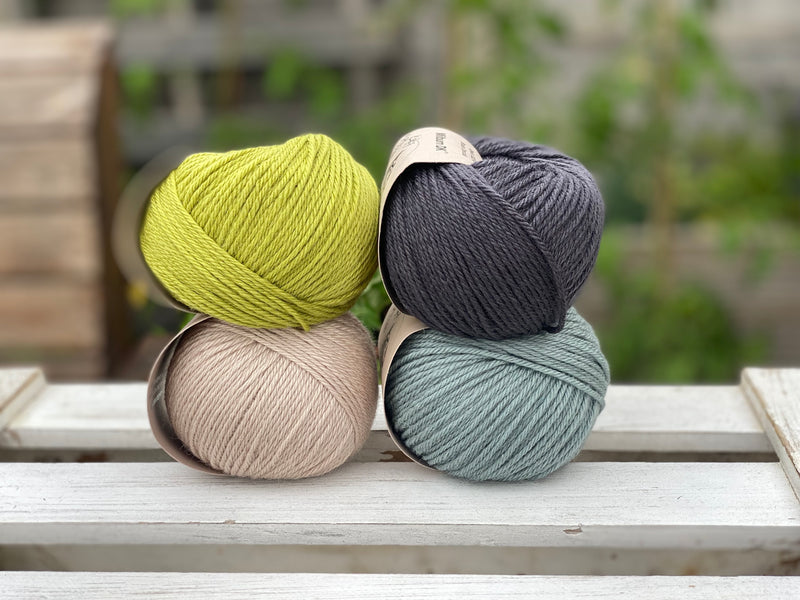 Four balls of yarn in two rows of two. There is a green ball, a dark grey ball, a beige ball and a blue-green ball.