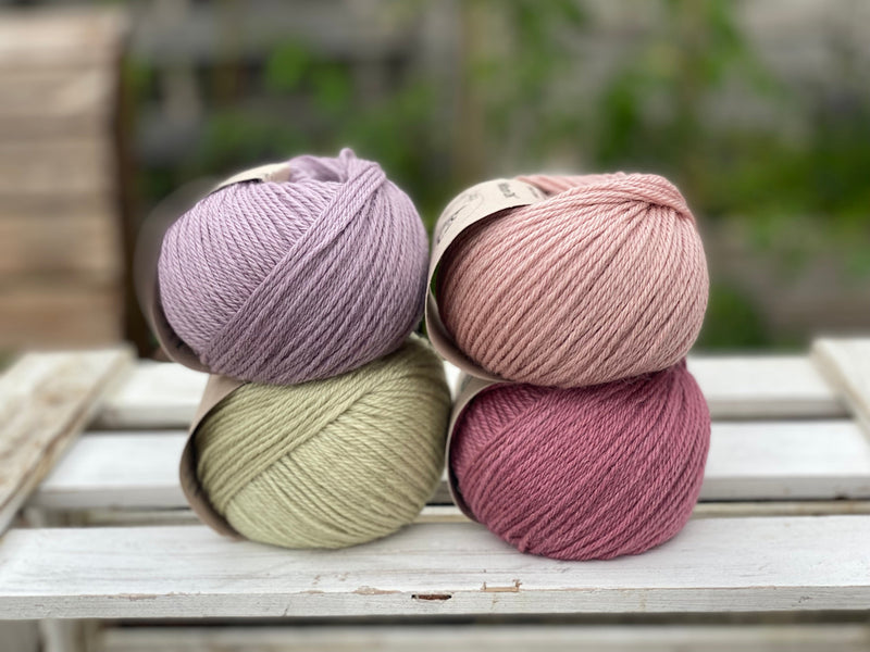 Four balls of yarn in two rows of two. There is a pale purple ball, a light pink ball, a light green ball and a dark pink ball.