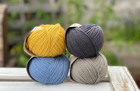 Four balls of yarn in two rows of two. There is a yellow ball, a dark grey ball, a blue ball and a grey ball.