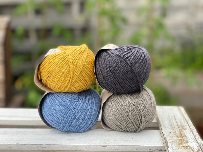 Four balls of yarn in two rows of two. There is a yellow ball, a dark grey ball, a blue ball and a grey ball.