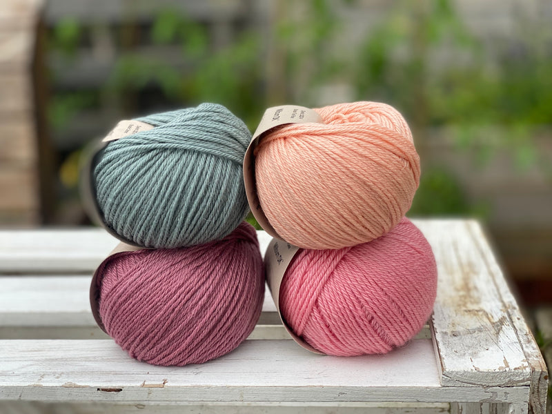 Four balls of yarn in two rows of two. There is a blue-green ball, a peachy orange ball, a dark pink ball and a bright pink ball.