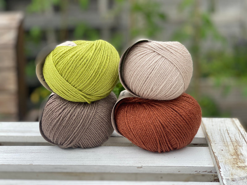 Four balls of yarn in two rows of two. There is a beige ball, a brown ball, a reddish-brown ball and a green ball.
