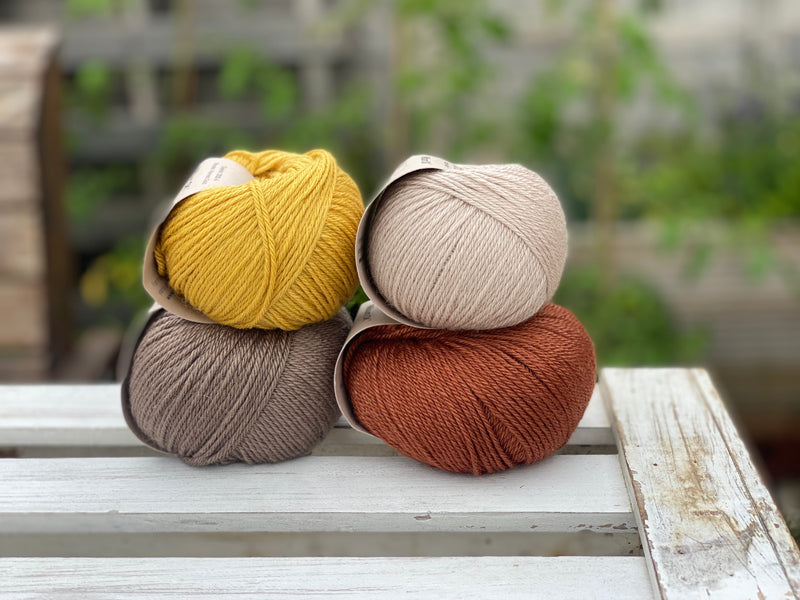 Four balls of yarn in two rows of two. There is a beige ball, a brown ball, a reddish-brown ball and a yellow ball.