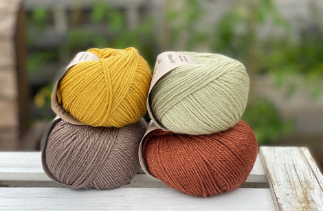 Four balls of yarn in two rows of two balls. There is a yellow ball, a brown ball, a pale green ball and a reddish brown ball.