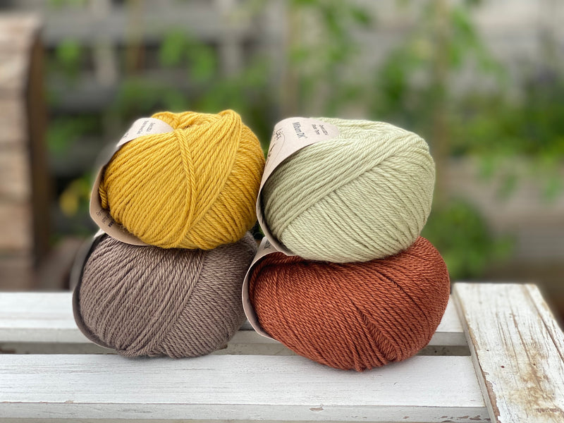 Four balls of yarn in two rows of two balls. There is a yellow ball, a brown ball, a pale green ball and a reddish brown ball.