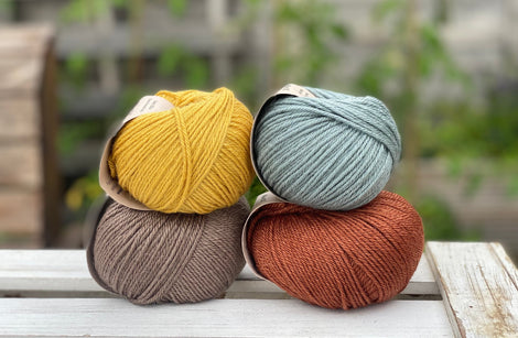 Four balls of yarn in two rows of two balls. There is a yellow ball, a brown ball, a blue-green ball and a reddish brown ball.