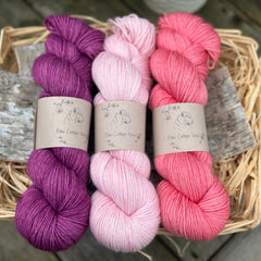 Three skeins of yarn in shades of pink and purple