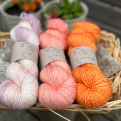 Three skeins of yarn in shades of orange, pink and cream