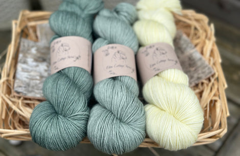 Three skeins of yarn in shades of blue-green and pale yellow