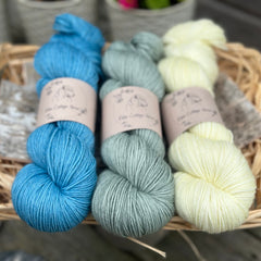 Three skeins of yarn. From left to right - a bright blue skein, a light blue-green skein and a pale yellow skein