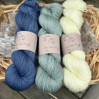 Three skeins of yarn. From left to right - a dark blue skein, a light blue-green skein and a pale yellow skein