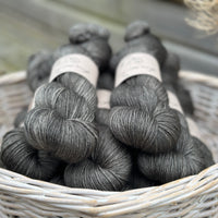 A white wicker basket containing several skeins of dark grey yarn
