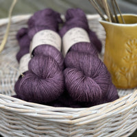 Five skeins of dark purple yarn in a white wicker basket