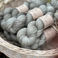 A white wicker basket containing several skeins of grey yarn