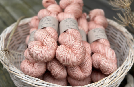 A white wicker basket containing several skeins of pink yarn