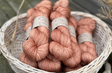 A white wicker basket containing several skeins of brownish pinky yarn