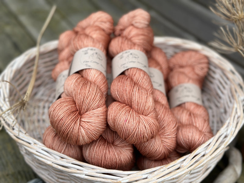 A white wicker basket containing several skeins of brownish pinky yarn