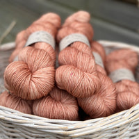 A white wicker basket containing several skeins of brownish pinky yarn