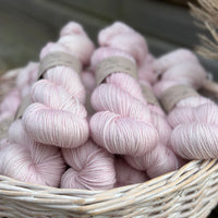A white wicker basket containing several skeins of pale pink yarn