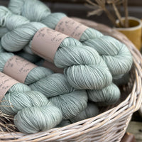 A white wicker basket containing several skeins of pale green yarn