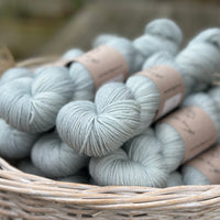 A white wicker basket containing several skeins of pale blue yarn