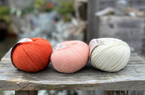 Three balls of yarn - from left to right an orange ball, a peachy orange ball and a cream ball