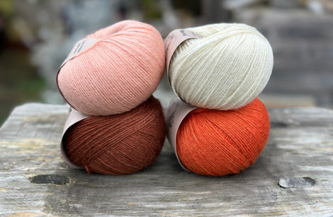 Four balls of yarn in two rows of two balls. The top row has a peachy orange ball and a cream ball. The bottom row has a reddish brown ball and an orange ball