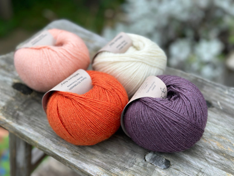 Four balls of yarn. From left to right there is a peachy pink ball, an orange ball, a cream ball and a dark purple ball.