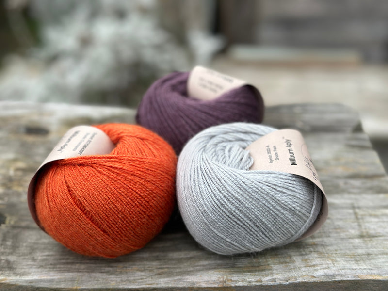 Three balls of yarn - one dark purple, one orange and one pale blue-grey