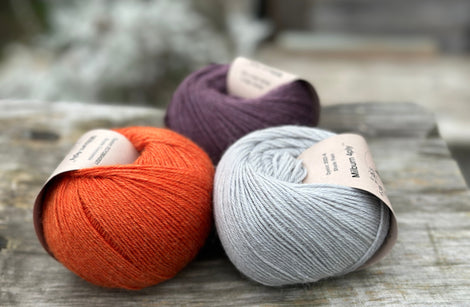 Three balls of yarn - one dark purple, one orange and one pale blue-grey