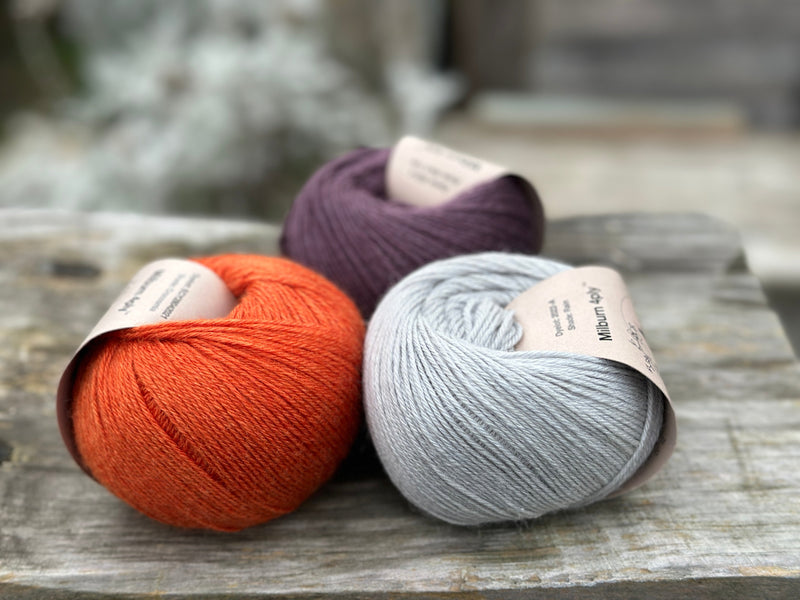 Three balls of yarn - one dark purple, one orange and one pale blue-grey